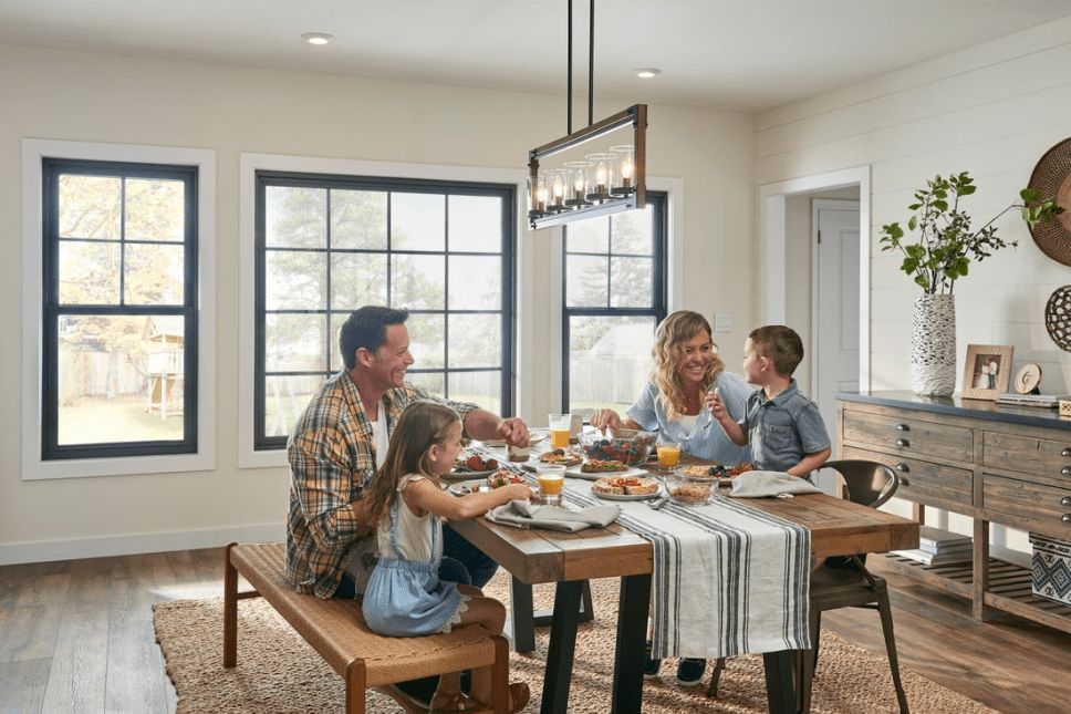 A happy family eating breakfast at the table in front of windows.