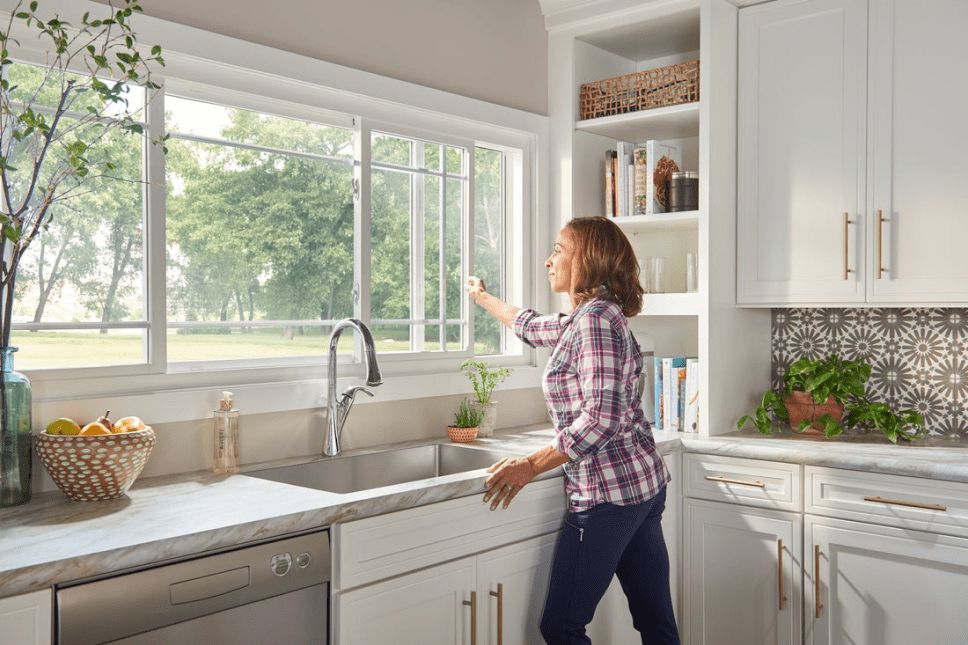 Woman smiling and opening a vinyl sliding window in a kitchen.