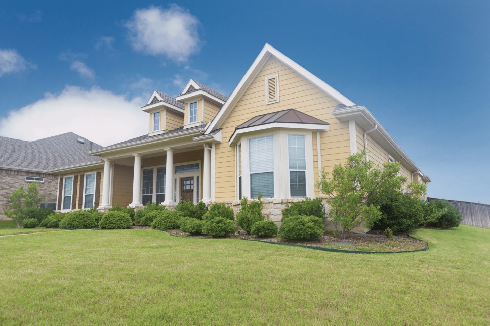 A home with yellow clapboard siding and bay windows with a large yard and clear blue skies.