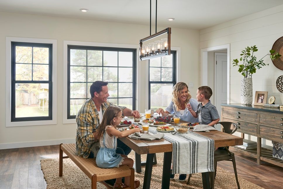 A dining room table in front of several casement windows with small awning windows above.