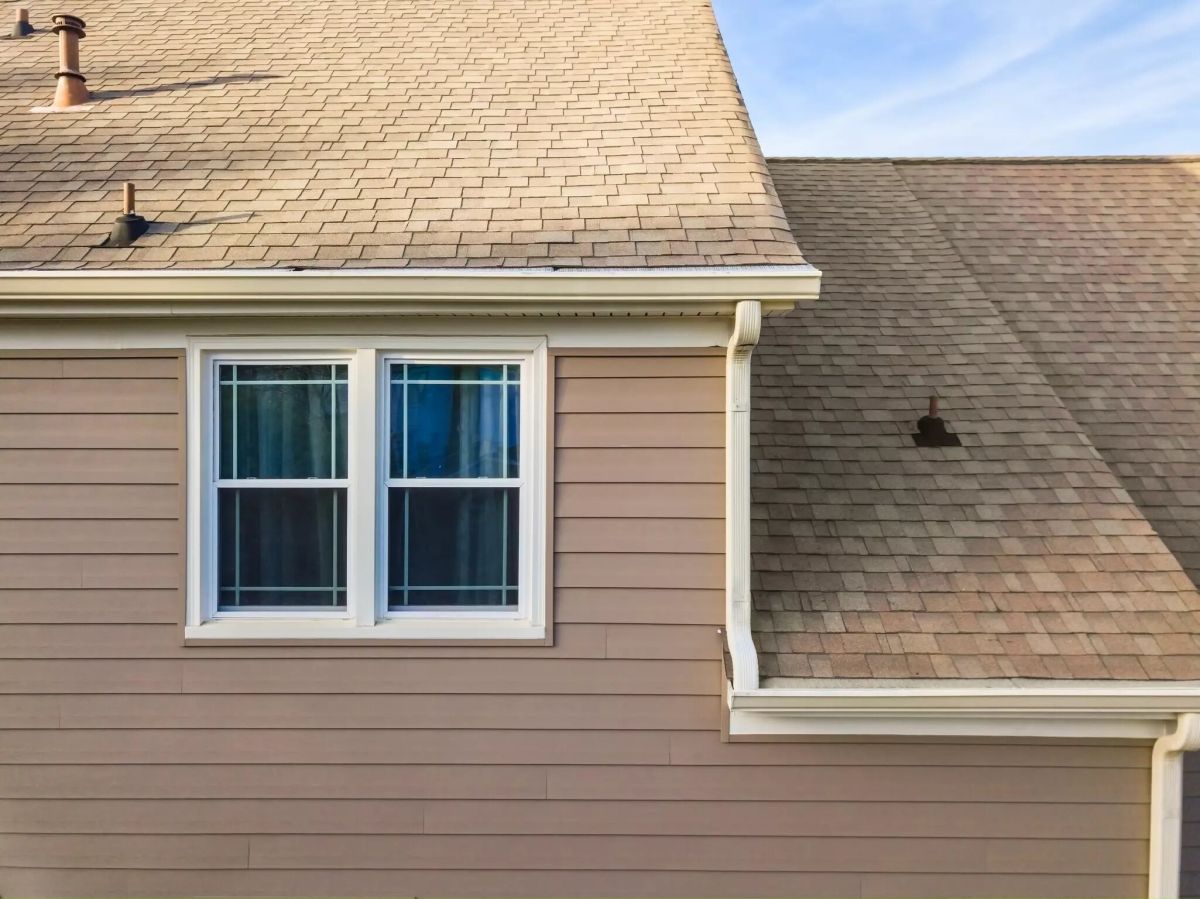 Tan horizontal lap siding on a home exterior with a white-trimmed window under a clear blue sky.